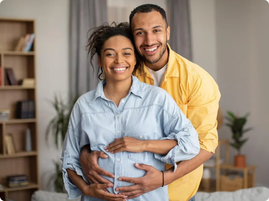 Casal sorrindo abraçado, com as mãos sobre a barriga da gestante