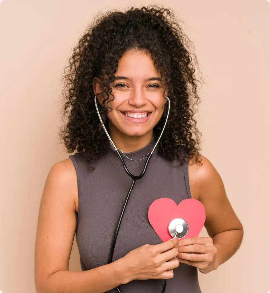 Mulher sorrindo com estetoscópio, segurando um coração de papel junto ao peito